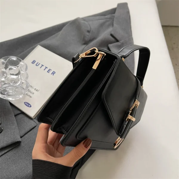 Hand holding black leather bag on gray suit.