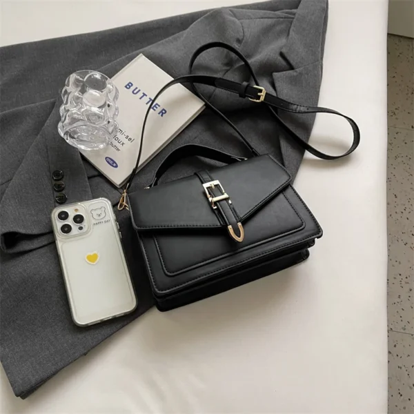 Black handbag, phone, book, and glass on grey fabric