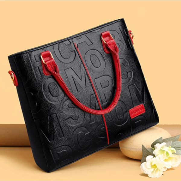 Black tote bag with red handles and embossed design.